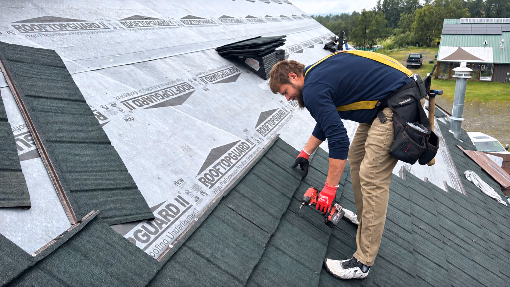 Fortress Roofing roofer in a harness fastening green stone-coated steel panels over underlayment