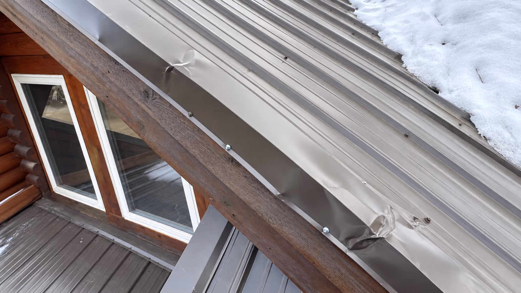 Metal eave trim crumpled and torn by sliding snow on a log home, Palmer