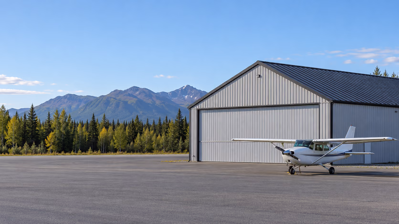 Aircraft hangar with a new standing seam metal roof, small plane parked in front, mountains behind