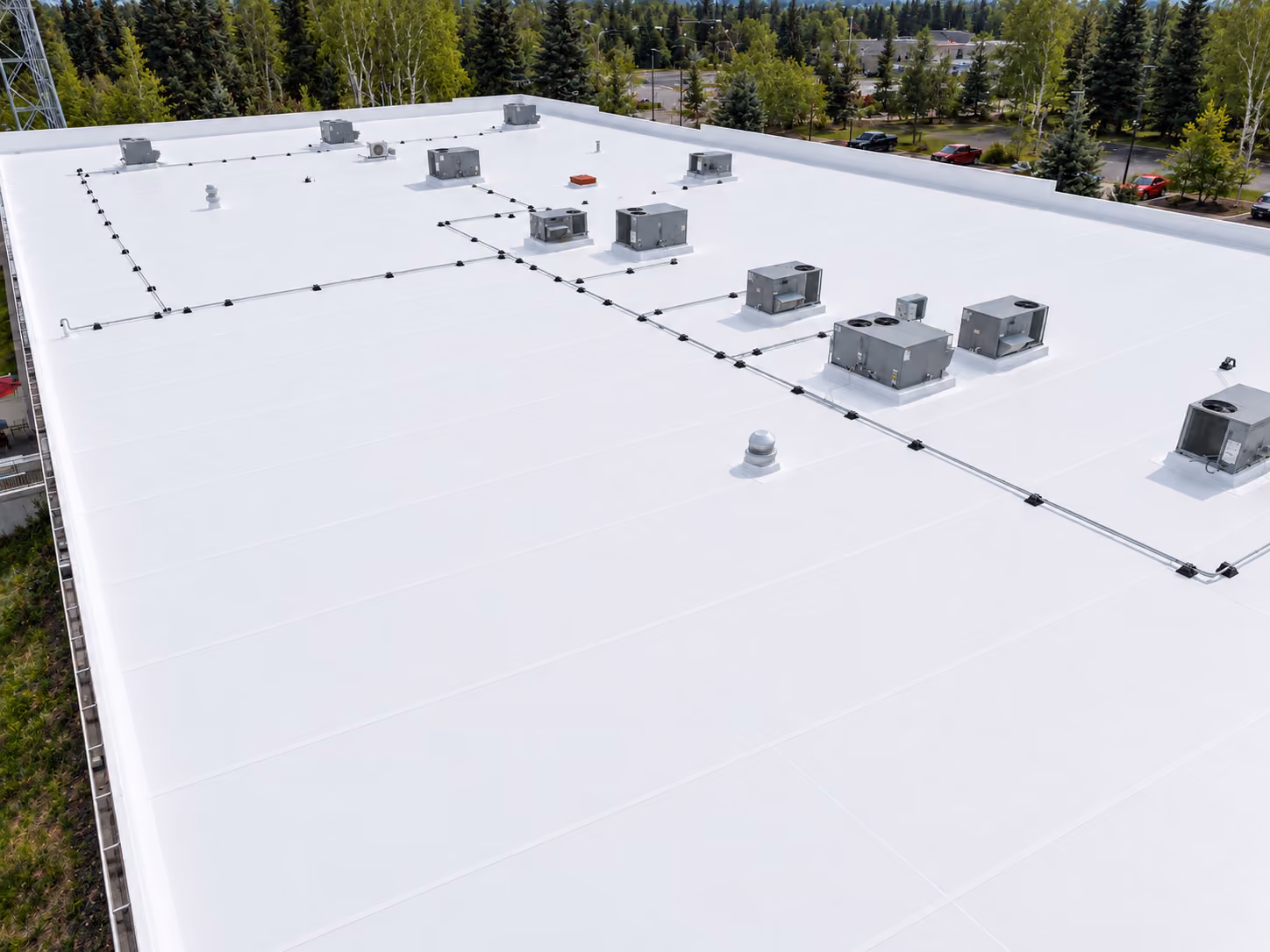 White low-slope membrane roof on a commercial building with rooftop units and a parapet, Anchorage